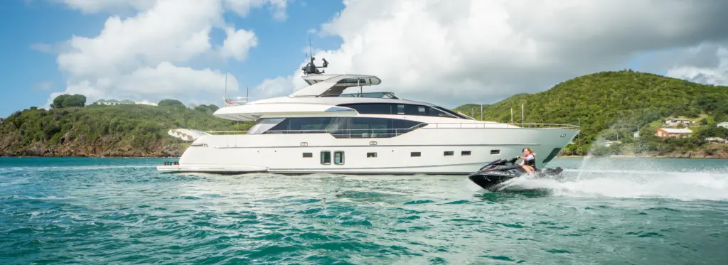 Person jet skiing alongside a luxury motor yacht anchored in a tropical Caribbean bay