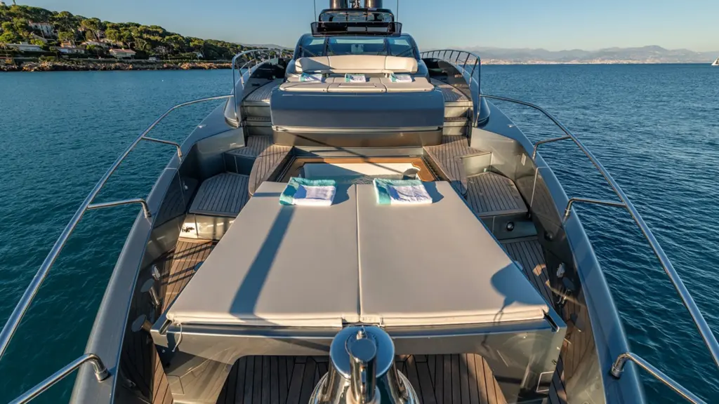 2024 Riva 110 Dolcevita TAKU foredeck featuring oversized sunpad with teak decking, wraparound seating, and stainless steel railings overlooking Mediterranean coastline