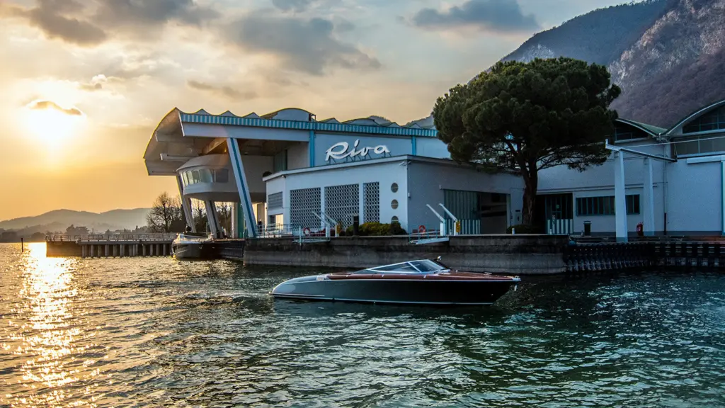 Classic Riva Aquarama wooden speedboat at sunset in front of iconic Riva headquarters building on Lake Iseo, Italy with mountains in background