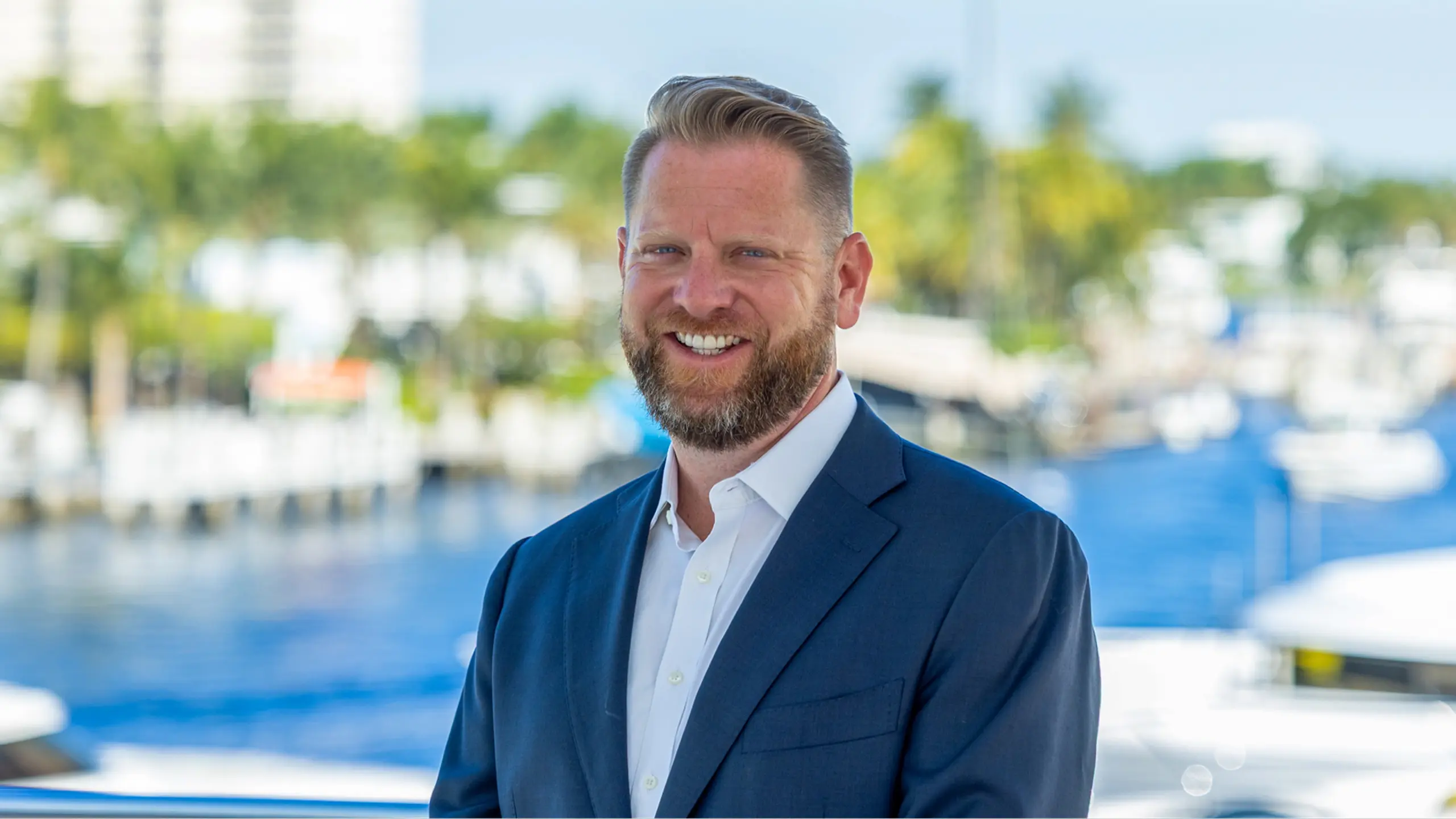 Patrick Hopkins, yacht broker at The Italian Yacht Group, wearing a navy suit and smiling at camera with marina backdrop in Fort Lauderdale