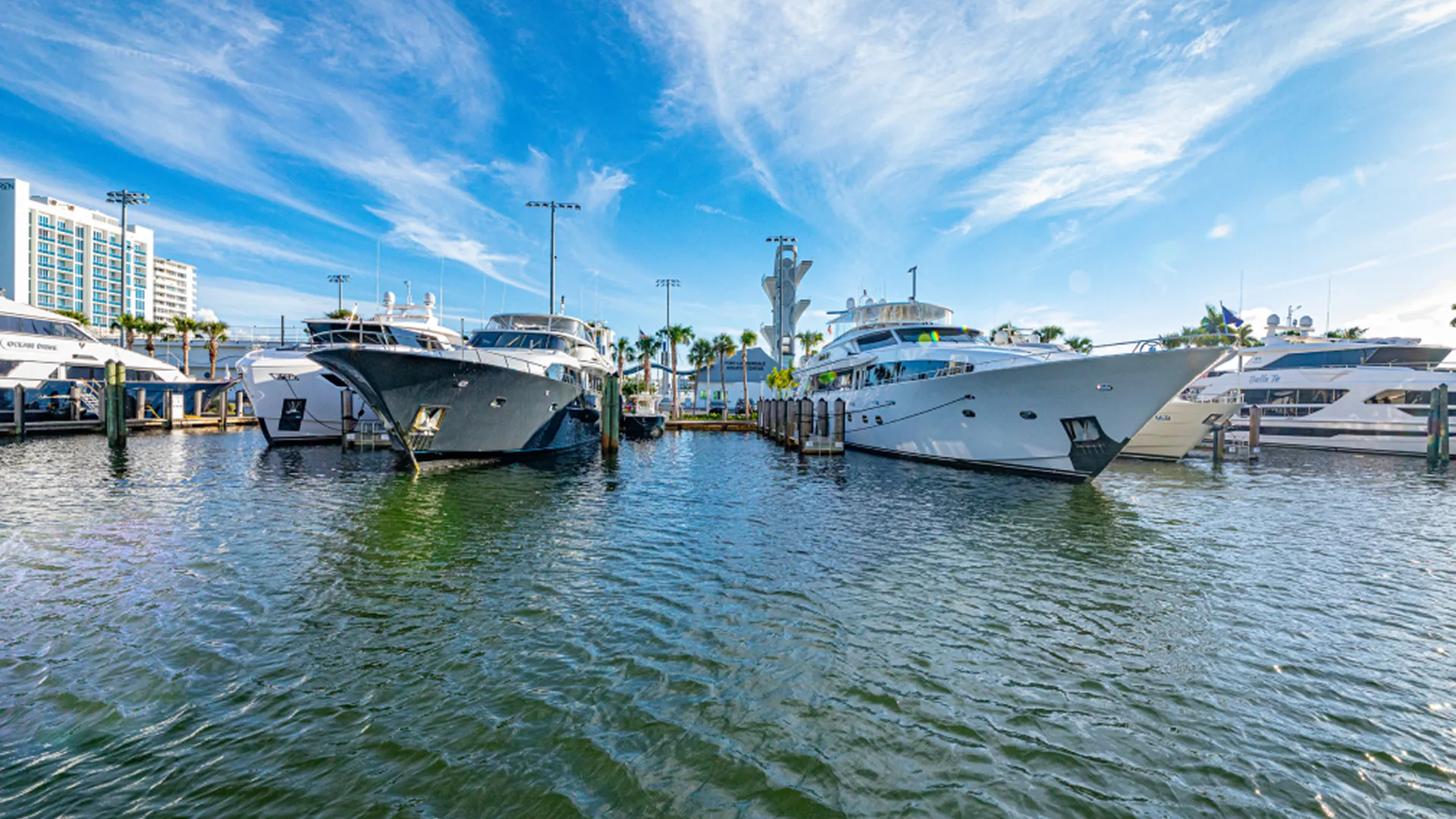 Motor yachts docked stern-in at Hall of Fame Marina in Fort Lauderdale under a bright blue sky with wispy clouds