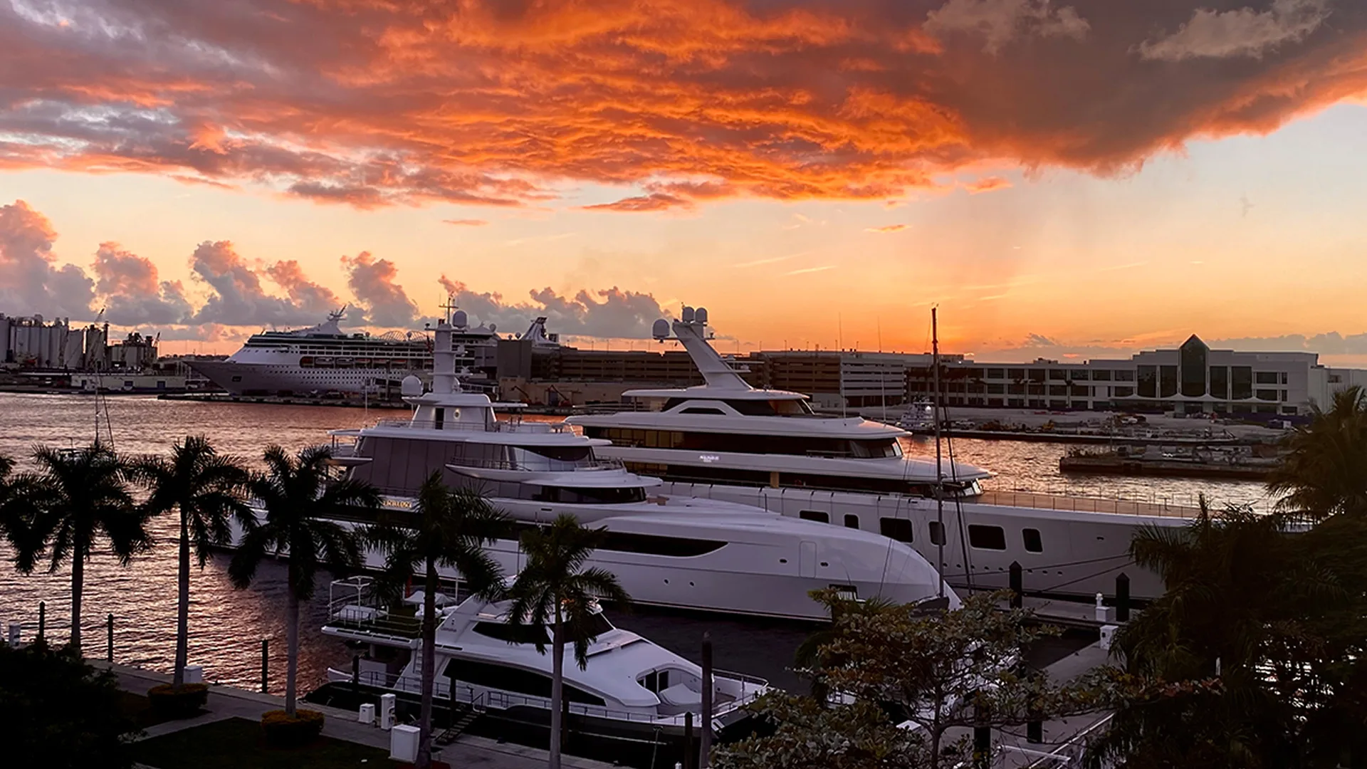 : Large yachts berthed at Pier 66 Marina in Fort Lauderdale at sunset, with palm trees and an orange sky overhead