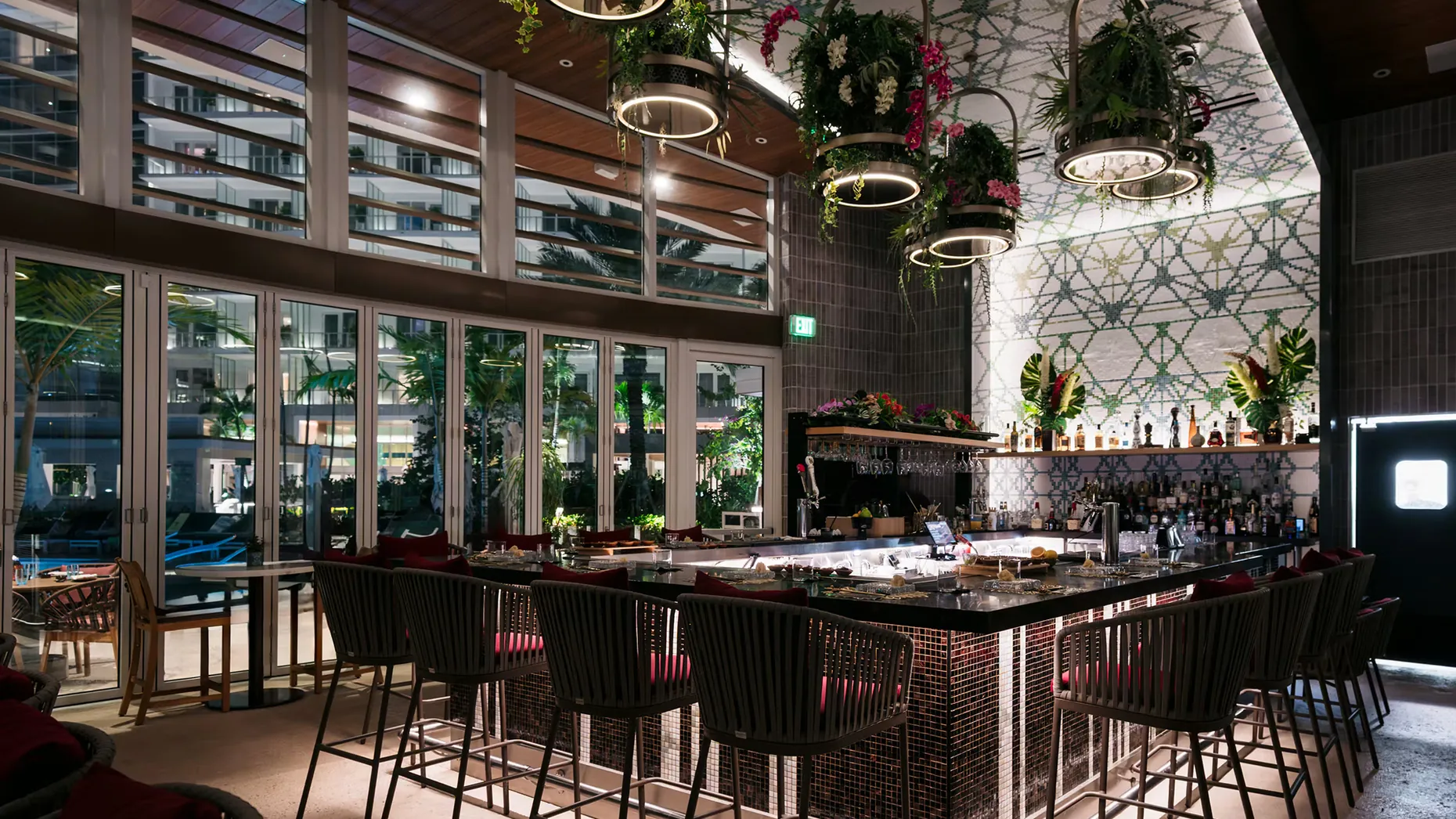 Sushi by Bou bar at Pier Sixty-Six with rope-style barstools, hanging floral planters and glass doors facing the pool