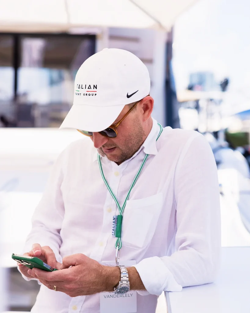 Yacht broker in an Italian Yacht Group cap checking his phone while preparing for a boat show